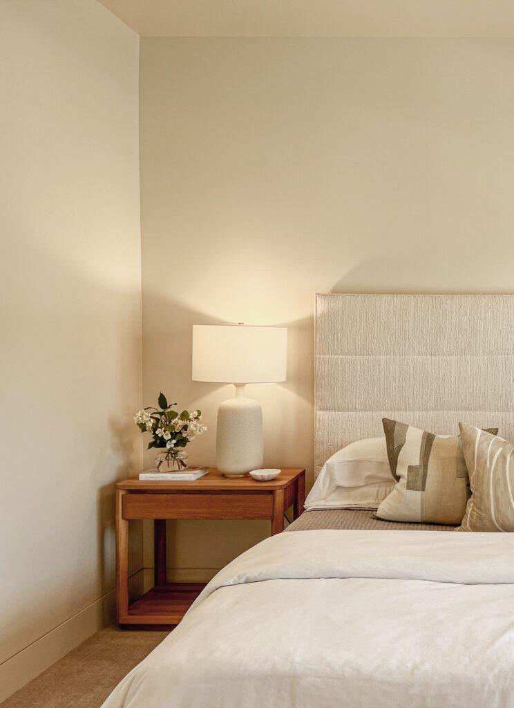 Bett mit Tagesdecke, Nachtschrank, warmem Licht, beigefarbener Tagesdecke Home Staging